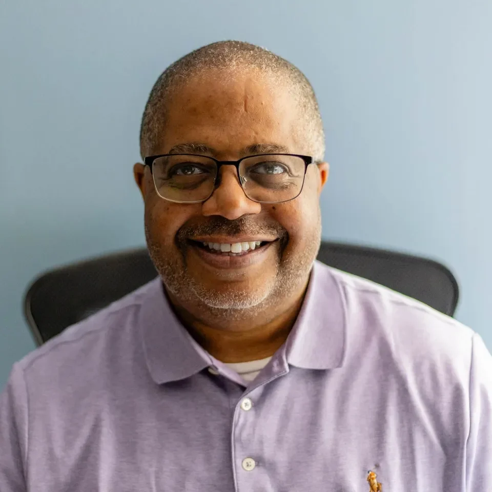 Smiling man wearing glasses and purple shirt.